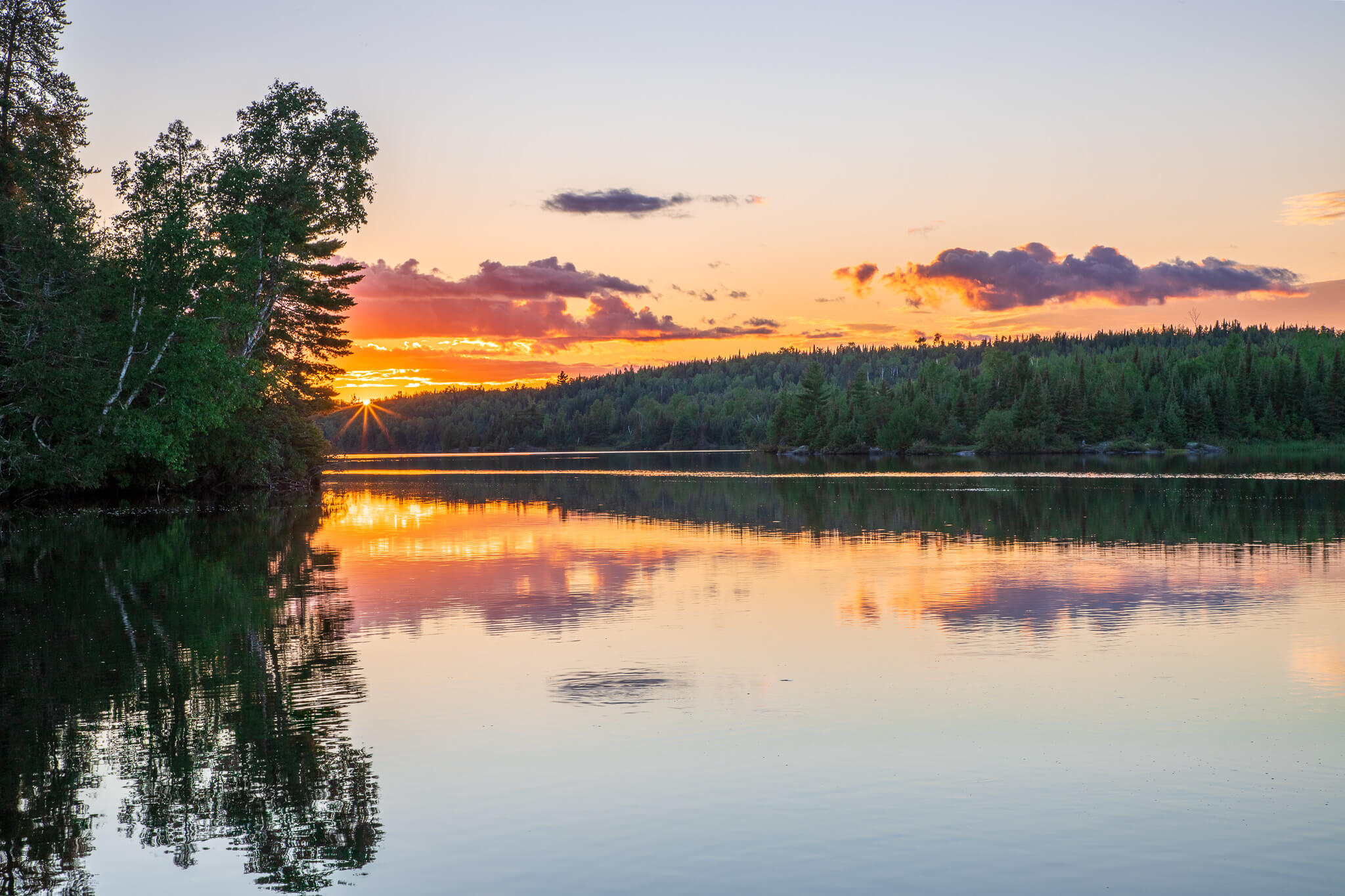 Perfect sunset reflection on still wilderness lake with sunburst through trees, Boundary Waters Minnesota