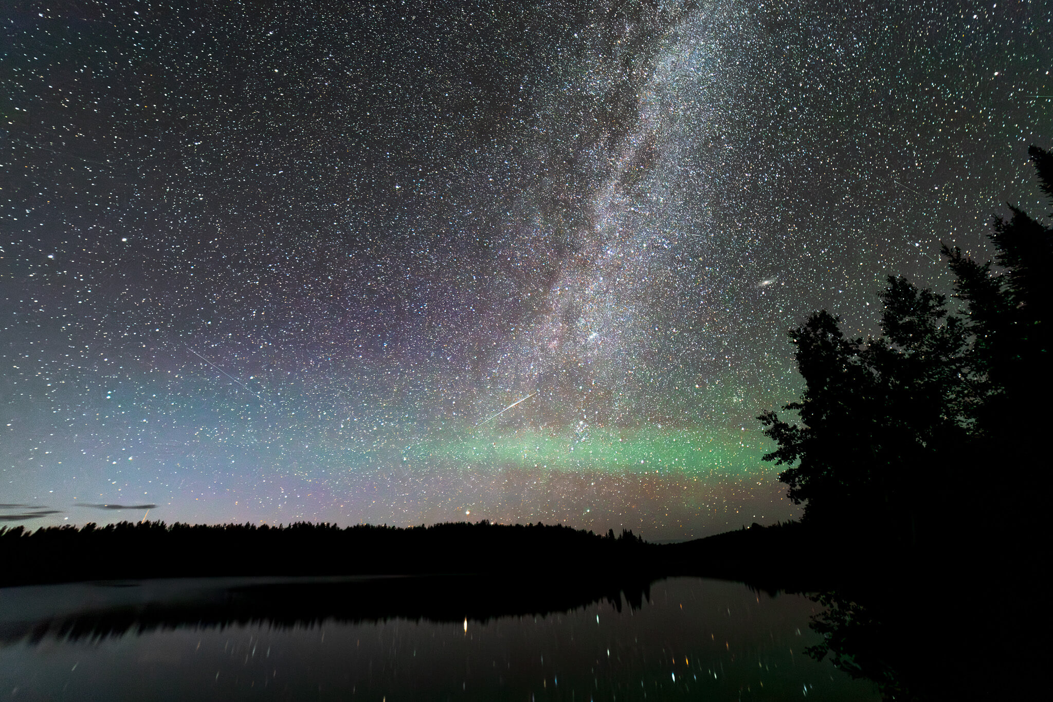 Milky Way with green northern lights glow reflected in still lake, Boundary Waters Minnesota