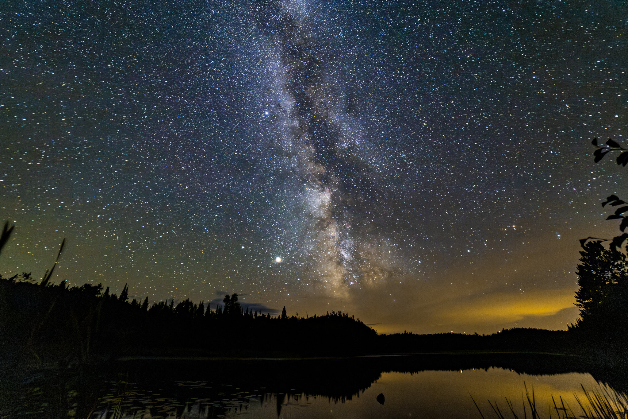 Milky Way rising vertically over wilderness lake shoreline with amber horizon glow, Boundary Waters Minnesota