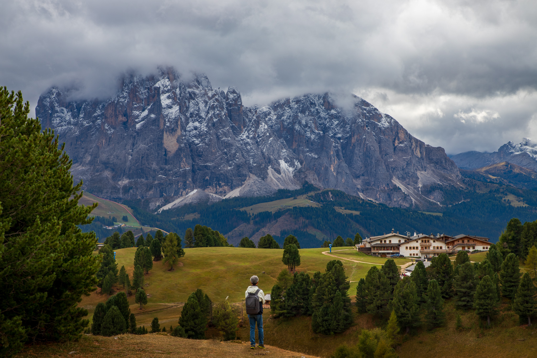 Solo hiker contemplating Sassolungo massif from alpine meadow
