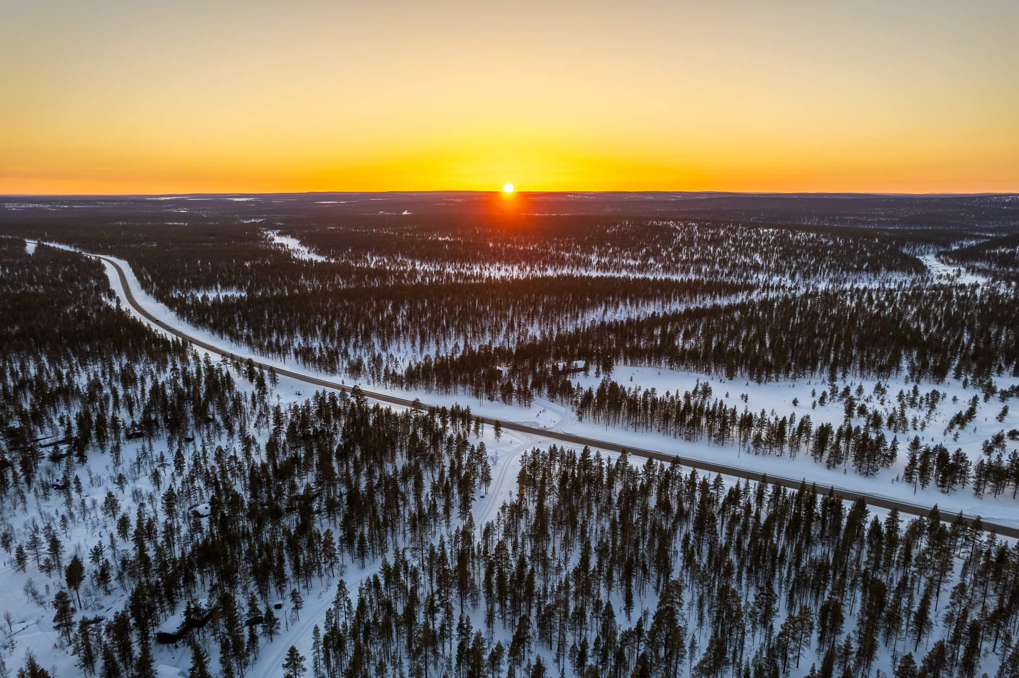 Aerial wide view of snow forest and winding roads at golden sunset, Lapland