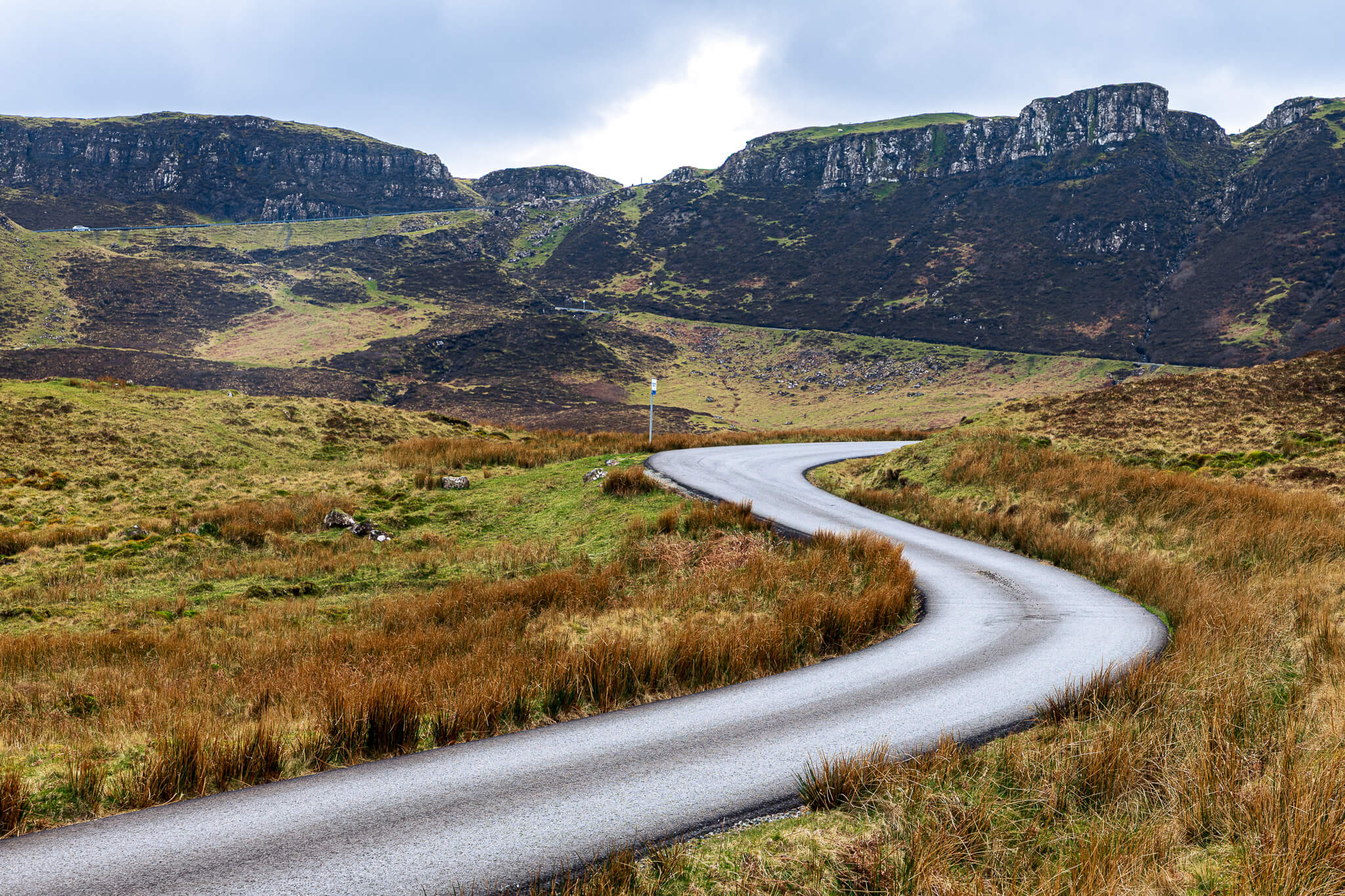 Winding single-track Highland road curving into dramatic rocky mountains, Scotland