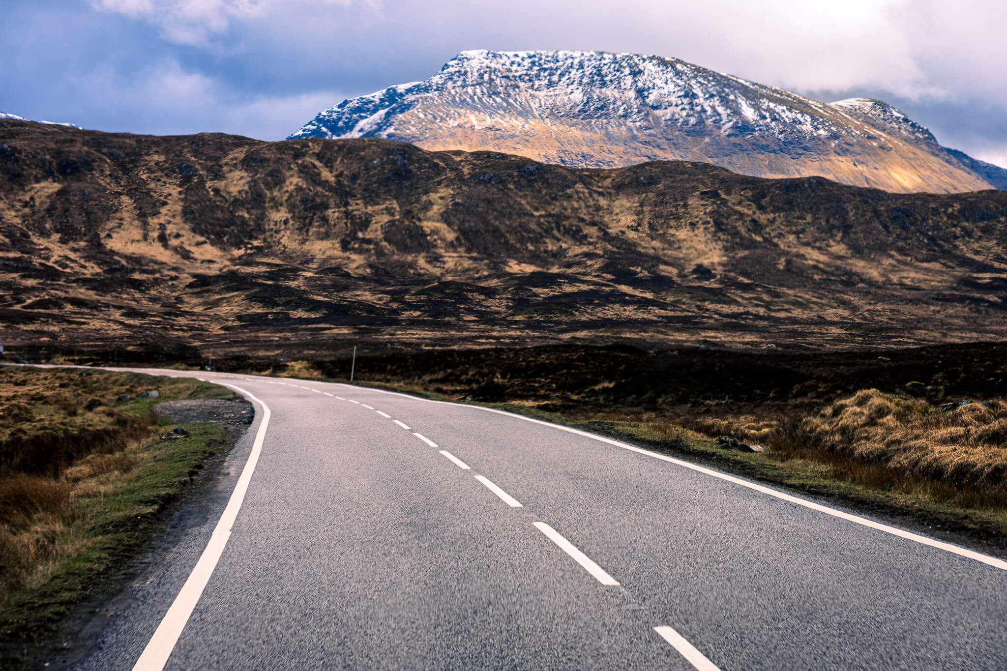 Empty Highland road leading toward snow-capped mountain, Scottish Highlands