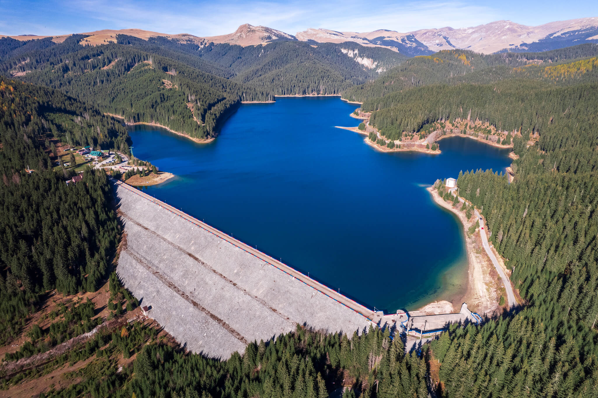 Aerial view of deep blue mountain reservoir dam surrounded by Carpathian peaks, Romania